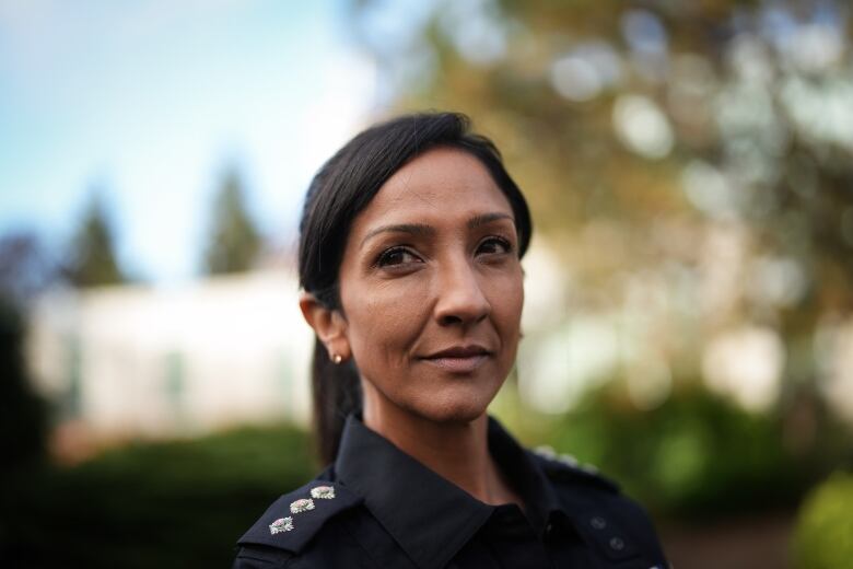 A brown woman in a police uniform looks away from the camera.