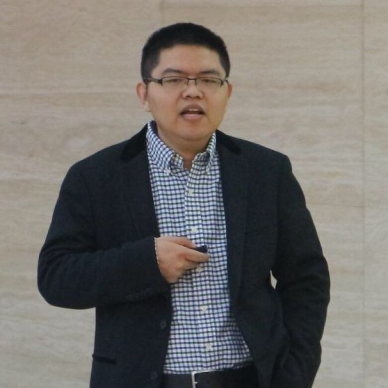 A man in a suit is talking, holding a clicker in one hand.