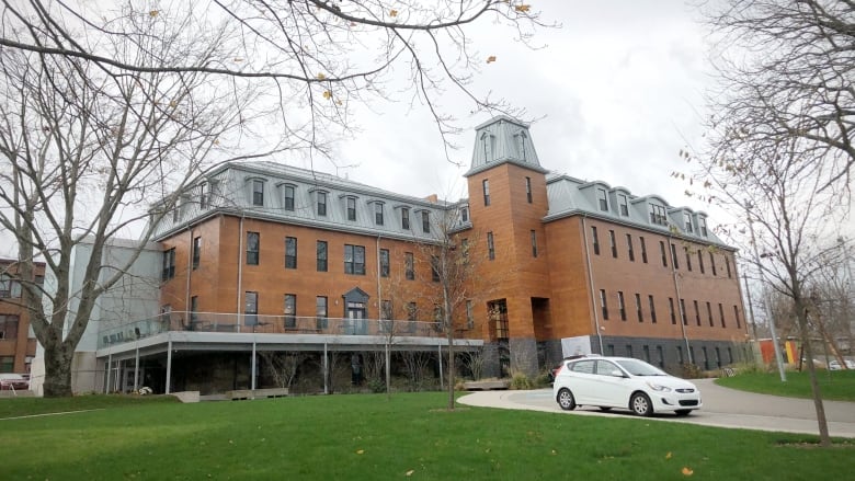 A four-storey red brick building is shown with grey siding on the top floor and a green grass lawn in the foreground.