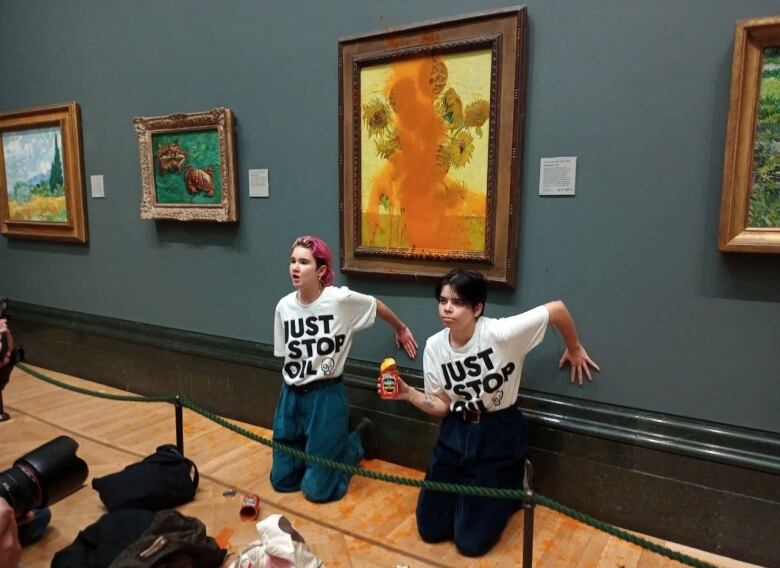 Two protesters are on their knees in front of a painting that has been vandalized with a can of soup.