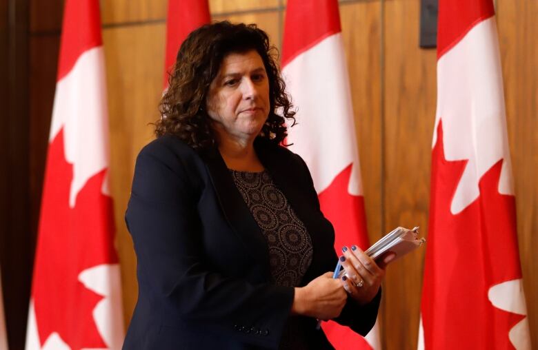 A women wearing a blue suit walks in front of a row of Canadian flags.