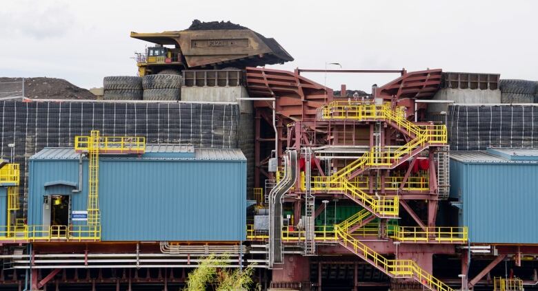 Buildings and stairs are shown in the foreground while a large dump truck waits to dump its load on top.