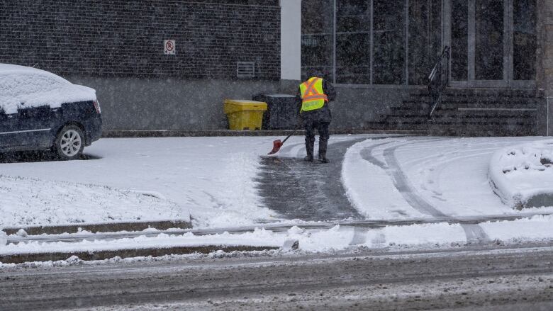 Someone shovels a driveway while wearing a reflective vest.