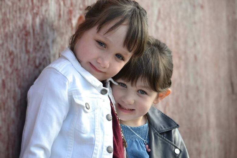 A portrait shows two smiling young girls standing outside in front of a stone wall.