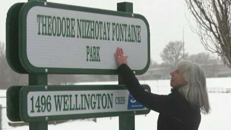 A woman reaches out to touch a white sign with green lettering reading 