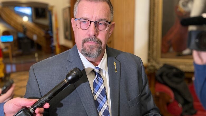  Man wearing glasses and a goatee stands in from of reporters at the legislature.