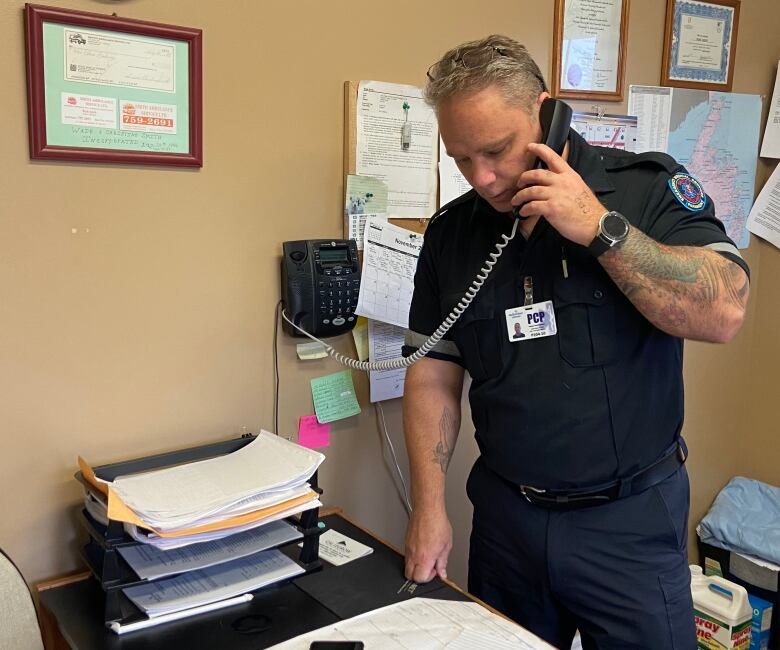 A paramedic standing over a desk in a small office while on the phone. 