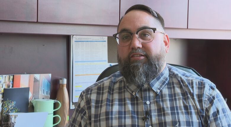 A portrait of a man sitting at a desk with glasses and a long beard.