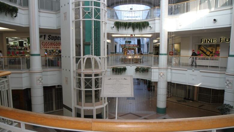 A view from a balcony looking at a white-and-pastel coloured mall with skylights and a glass elevator.