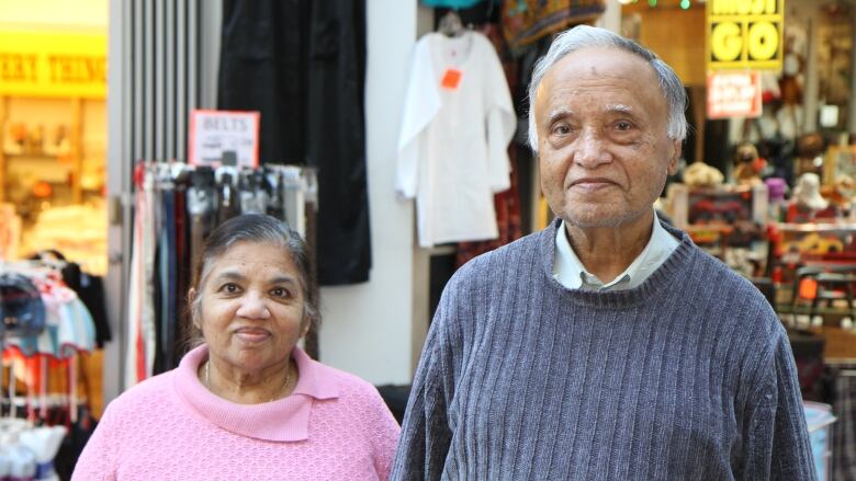 A person in a pink sweater smiles next to a taller person in a dark grey sweater in front of a store where a sign reads 'Everything must go.'