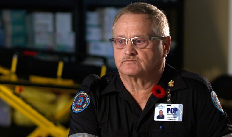 A paramedic looks contemplative, sitting with a strecher and medical supplies in the background. 