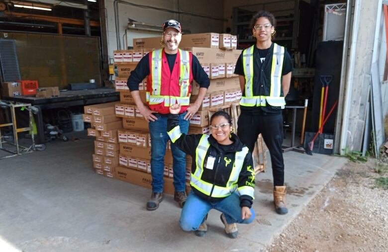 People dressed in construction worker gear stand in front of cardboard boxes.