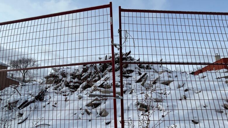 A pile of debris, covered in snow, can be seen behind a fence.