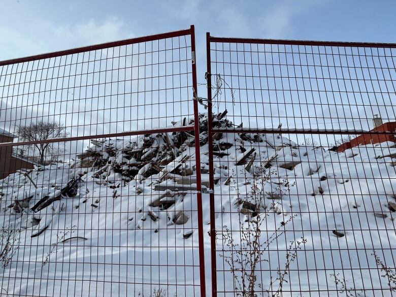 A pile of debris, covered in snow, can be seen behind a fence.