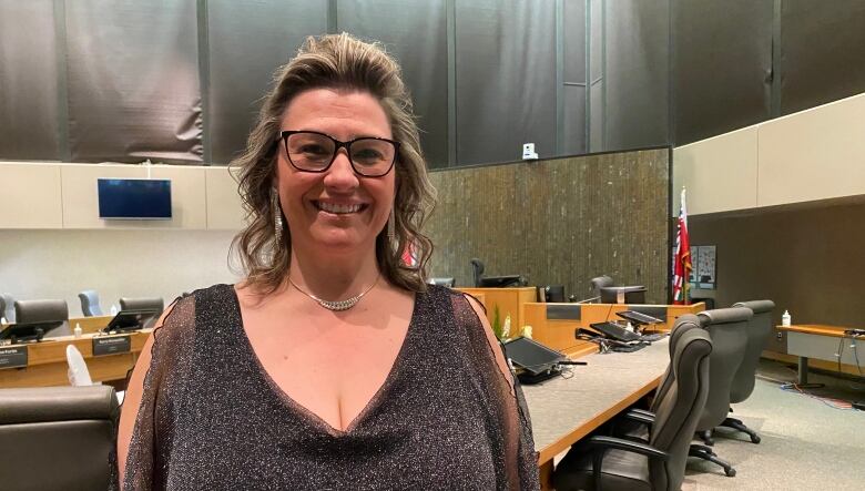 Natalie Labbe stands in the council chamber, with empty seats seen behind her. 