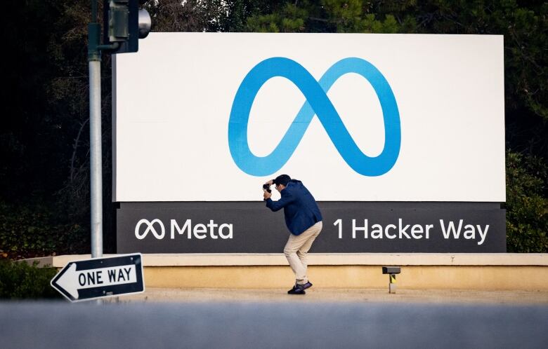 A man walks in front of a sign with the corporate logo of Meta.