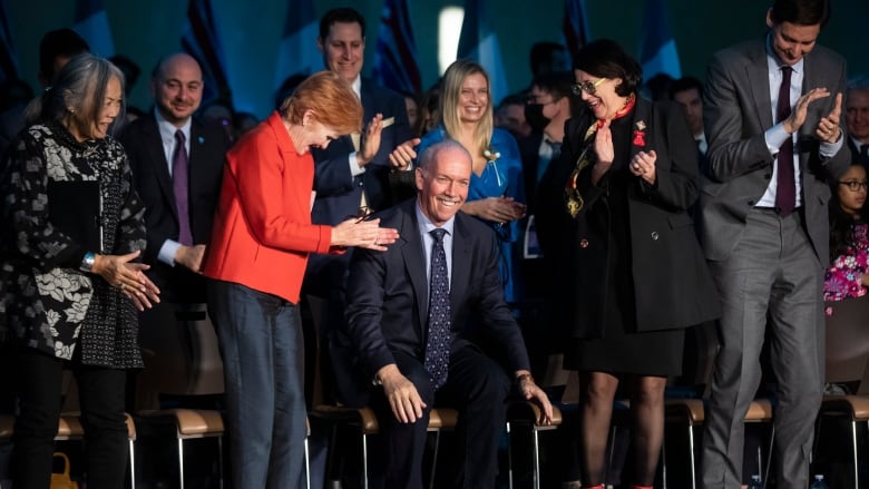 A group of people on a stage, smiling and applauding.