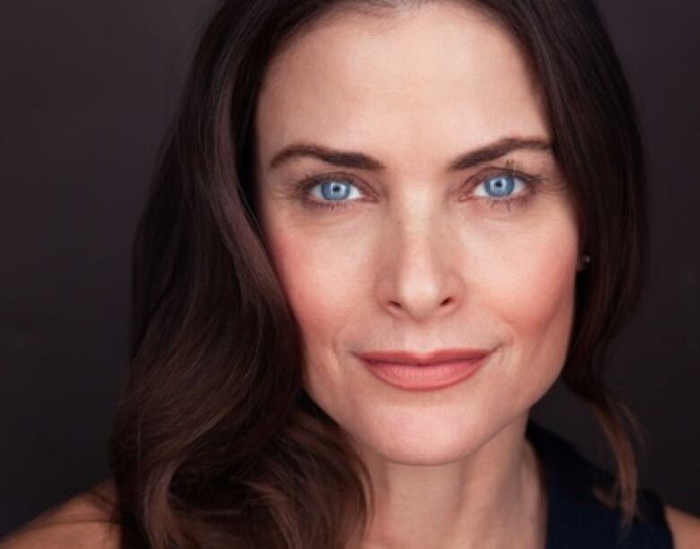 A woman with long brown hair and blue eyes smiles slightly as she looks at the camera.