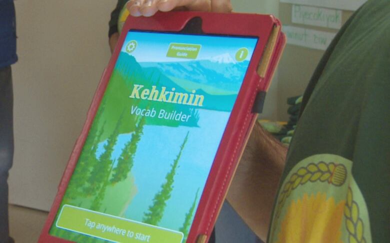 Some holds a tablet with a red case. The screen has an app open with trees in the background. The screen reads 