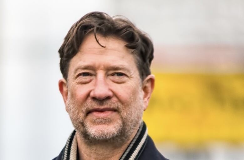 A man with brown hair and scruffy facial hair smiles. 