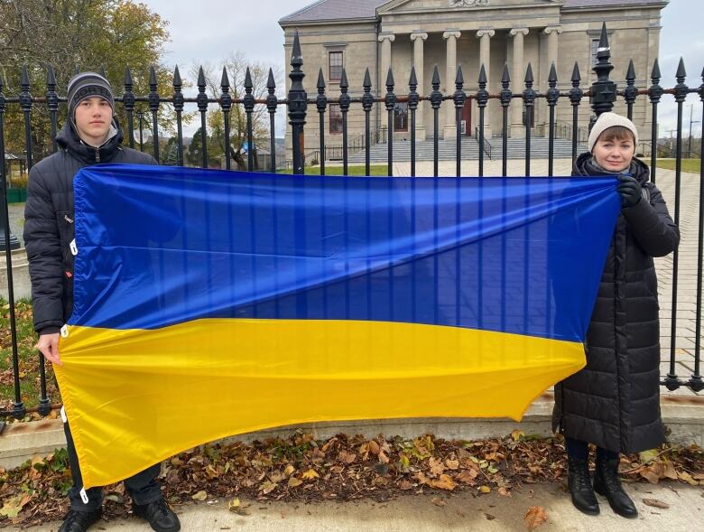 A man and woman wearing winter clothing stand outside holding up a blue and yellow flag.