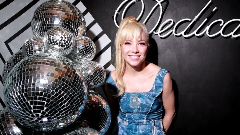 A photo of Canadian singer Carly Rae Jepsen beside a cluster of disco balls at a party celebrating the release of her 2019 album Dedicated.