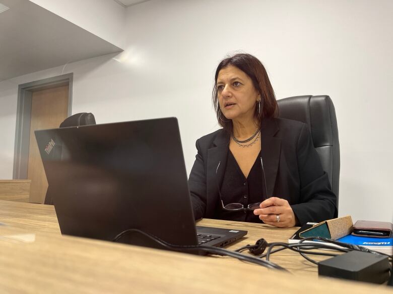 A woman sits at a laptop looking up.