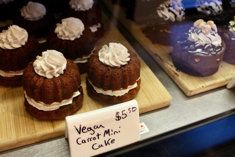 Small, medium-brown cakes with icing sandiwched in the middle and dolloped on top sit on a wooden board.