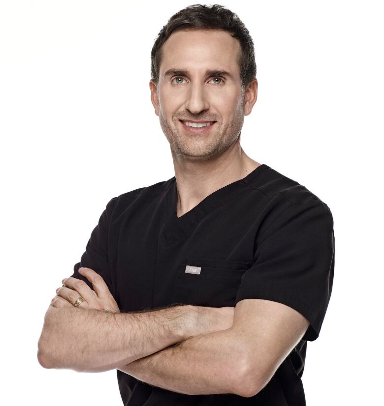 Professional photo shows a smiling white man wearing navy scrubs standing with crossed arms.