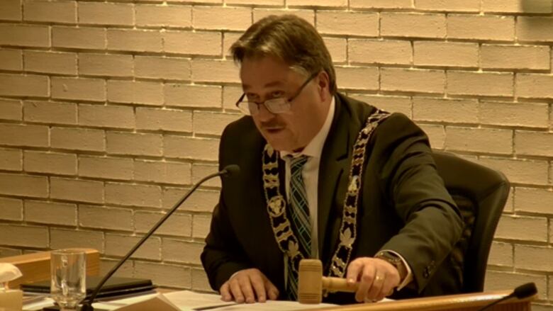 Chris Patrie bangs a gavel while sitting in the mayor's chair in Elliot Lake council chambers, wearing the chain of office 