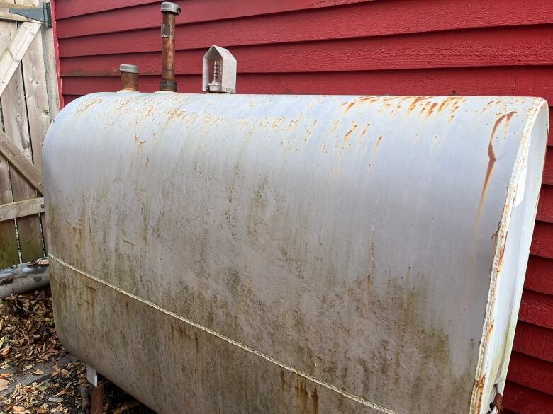 A grey home heating oil tank next to house with bright red siding.