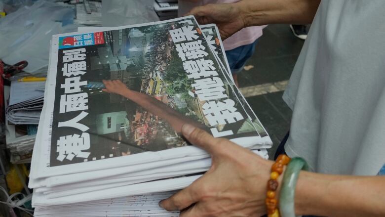 Hands holding a stack of Chinese language newspapers. 