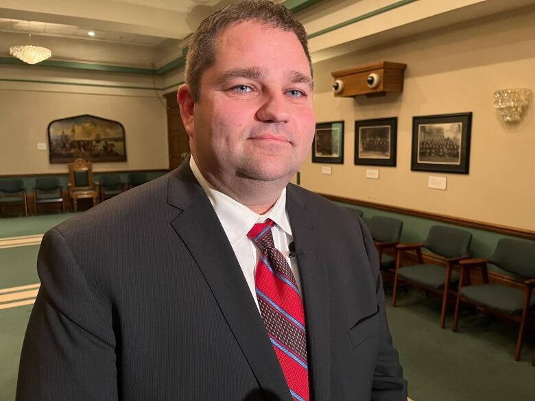 A head and shoulders shot of a person wearing a dark jacket and red and blue tie.