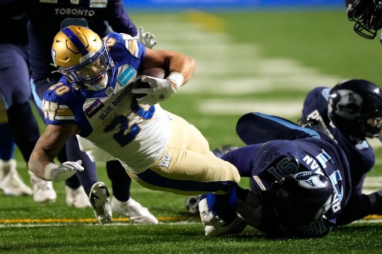 A pro football player tumbles to the ground clutching the football.