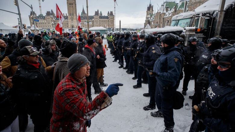 Protesters and police standing face to face in Ottawa, with the parliament building in the background.