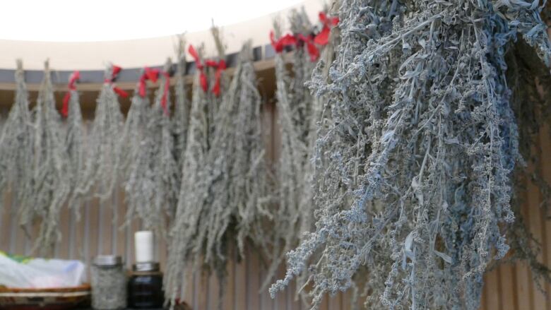 Dried herbs hang in bunches from the ceiling of a small round room.