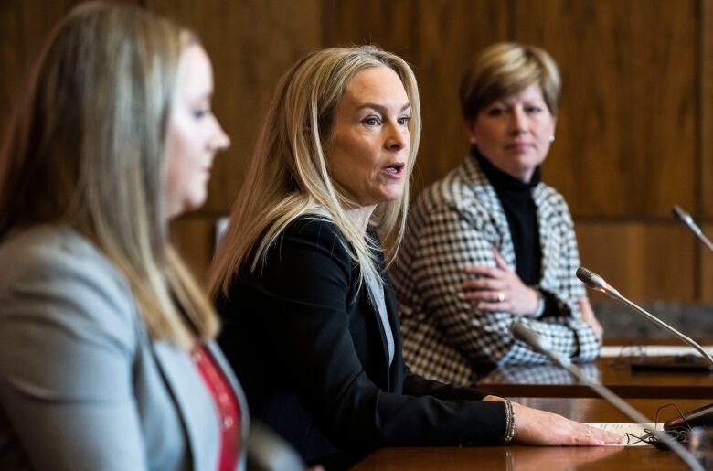 Someone sits and speaks at a desk during a news conference.