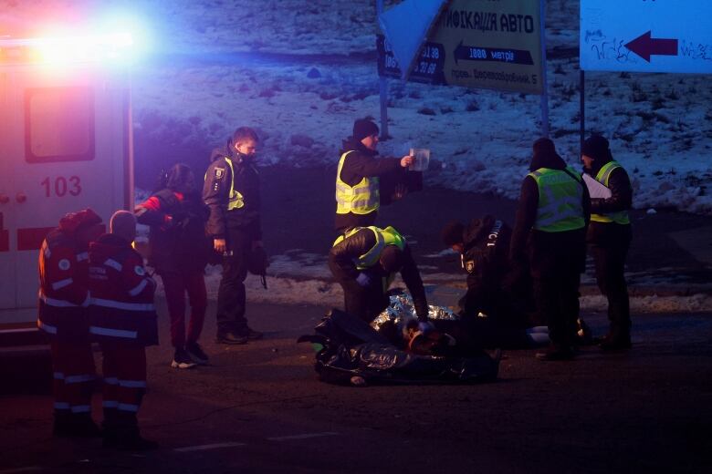 Emergency workers working on a person on a stretcher by the light of their ambulance.