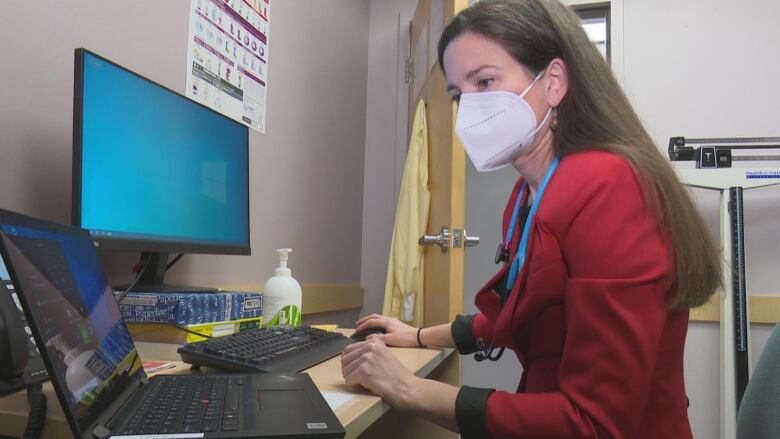 A female doctor sits in her office at a computer. 