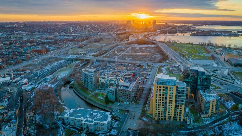 From above, the sun sets over the edge of a city's downtown, next to a river.