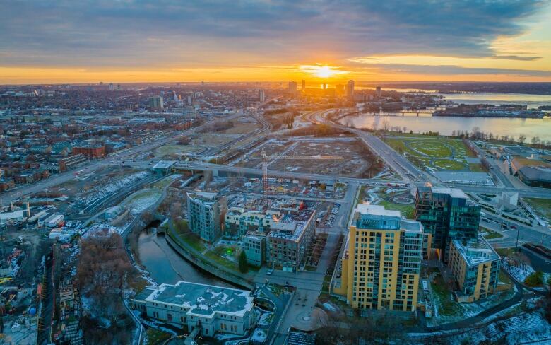 From above, the sun sets over the edge of a city's downtown, next to a river.