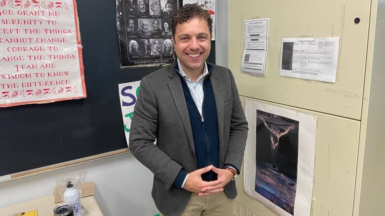 A man stands in a classroom, smiling at the camera. 