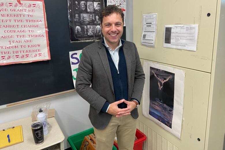 A man stands in a classroom, smiling at the camera. 