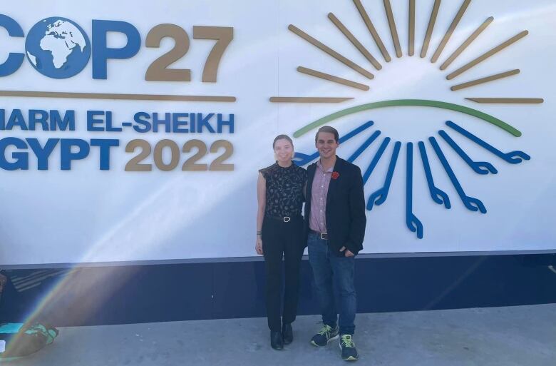 A man and woman smile in front of a sign promoting a climate conference.