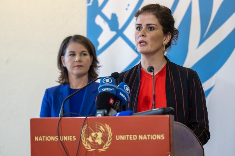 Two dark-haired women speak from a podium with 'United Nations' written on it.