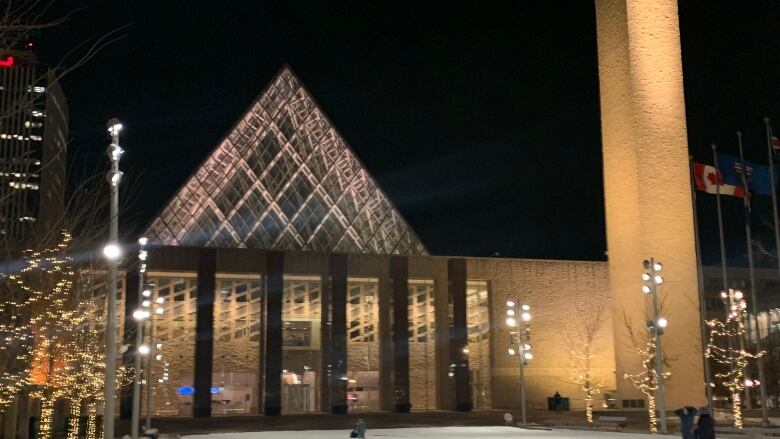 A view of the outside of Edmonton city hall, a building with a large glass pyramid on top, at night.