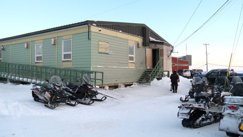 A green building with ski-doos parked outside 