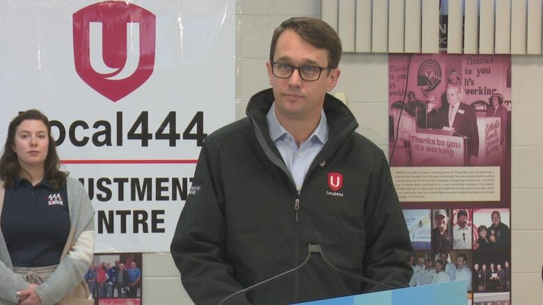 A politician stands behind a podium in a room with union signage. 