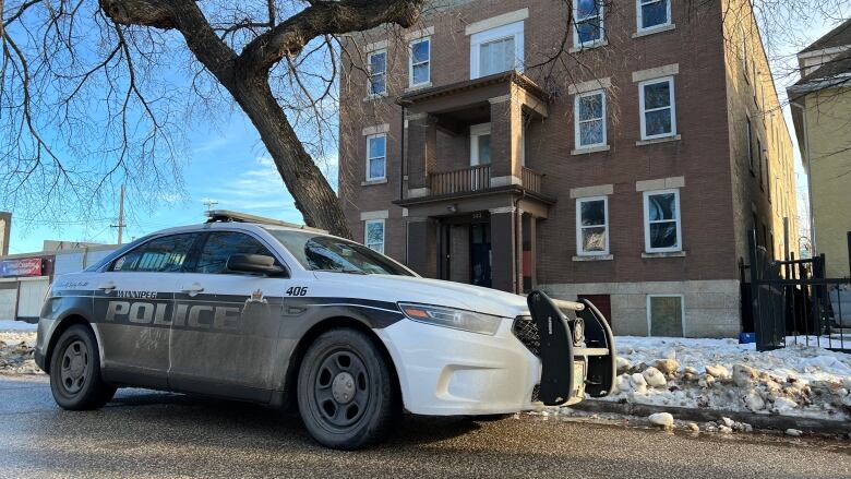 A police car is parked in front of an three-storey brown brick apartment block.