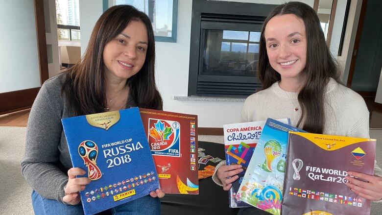 Two women hold up sticker albums.